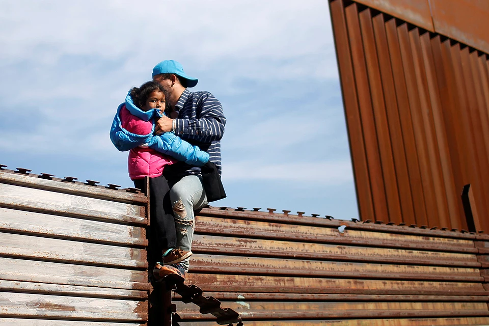 Мигрант изучает варианты перебраться через забор на границе США и Мексики.