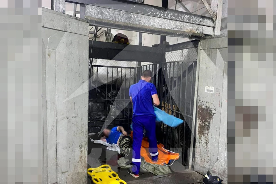 Медик оказывает первую помощь рабочим, пострадавшим в результате падения лифта в складском помещении на Иловайской улице.