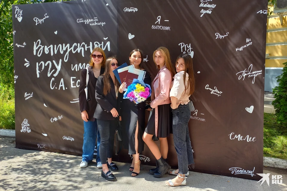 Выпускники РГУ фотографируются на фоне баннера.