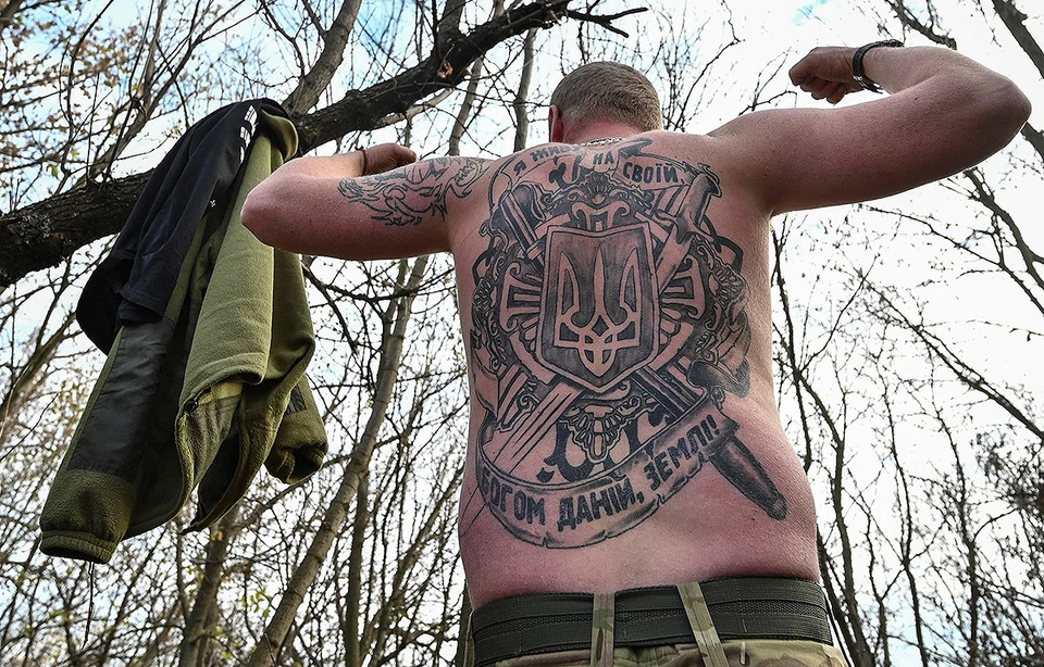 Боец ВСУ демонстрирует журналистам татуировку на фронтовых позициях в Запорожской области.