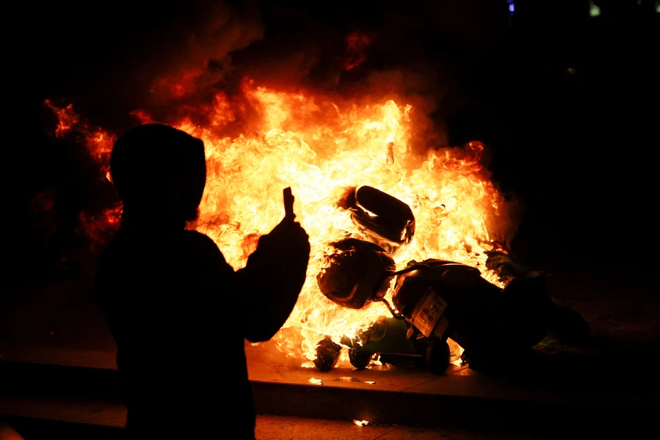 Во Франции не утихают протесты против пенсионной реформы правительства Макрона. На фото - участник погромов фотографирует горящий скутер в Париже. Фото: REUTERS